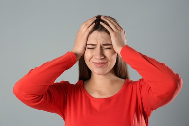 Young woman suffering from migraine on grey background