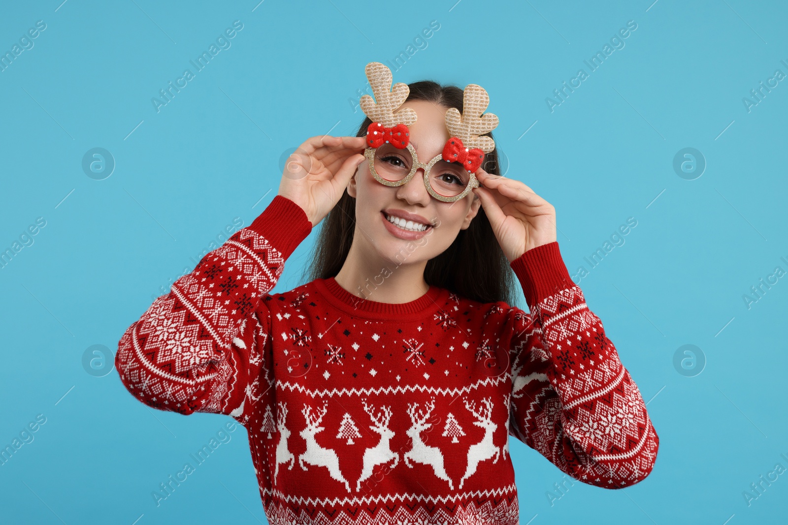 Photo of Happy young woman in Christmas sweater and funny glasses on light blue background