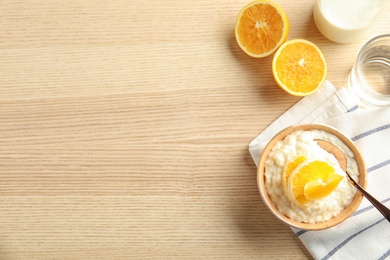 Photo of Creamy rice pudding with orange slices in bowl served on wooden table, top view. Space for text