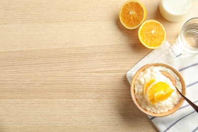 Creamy rice pudding with orange slices in bowl served on wooden table, top view. Space for text