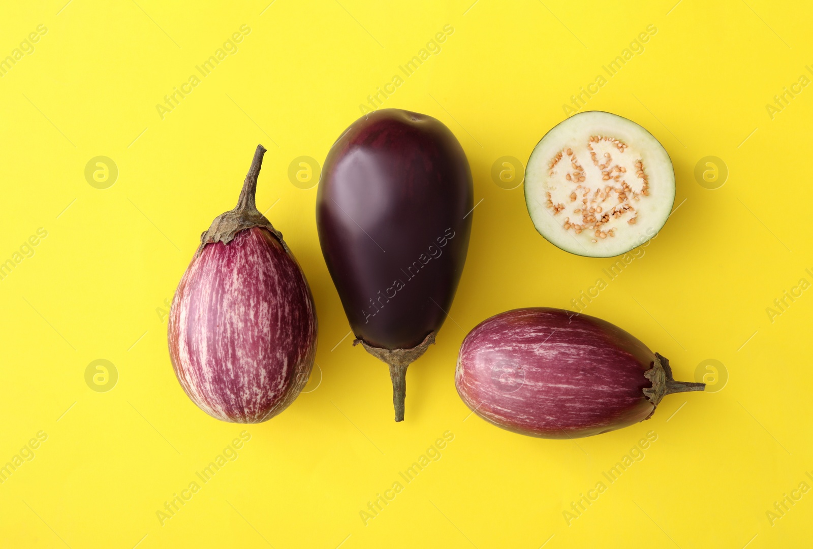 Photo of Cut and whole raw ripe eggplants on yellow background, flat lay