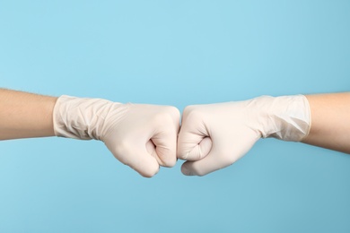 Photo of People in medical gloves doing fist bump on light blue background, closeup of hands