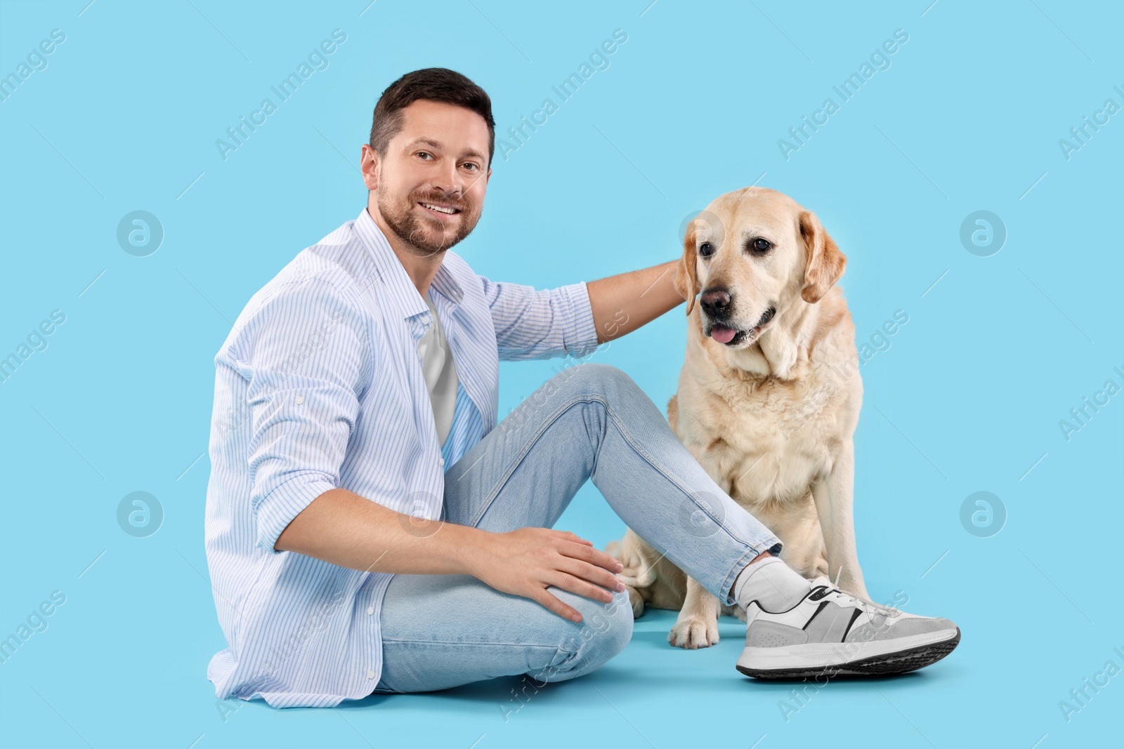 Photo of Man with adorable Labrador Retriever dog on light blue background. Lovely pet