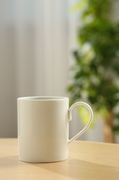 Photo of White mug on wooden table indoors. Mockup for design