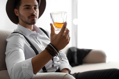 Photo of Young man with glass of whiskey sitting on sofa at home. Space for text