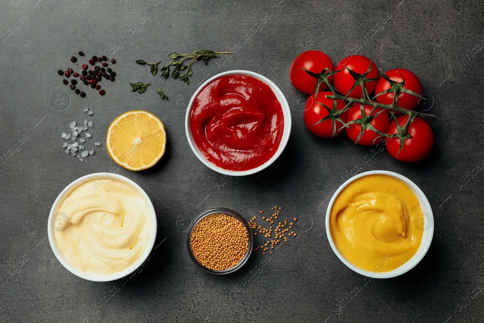 Photo of Flat lay composition with ketchup, mustard, mayonnaise and ingredients on grey table