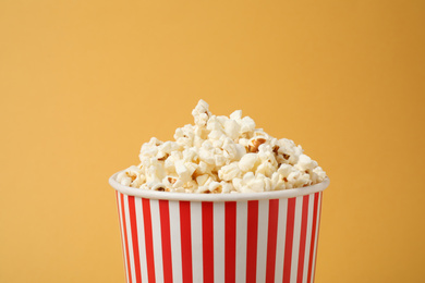 Photo of Delicious popcorn in paper cup on yellow background, closeup