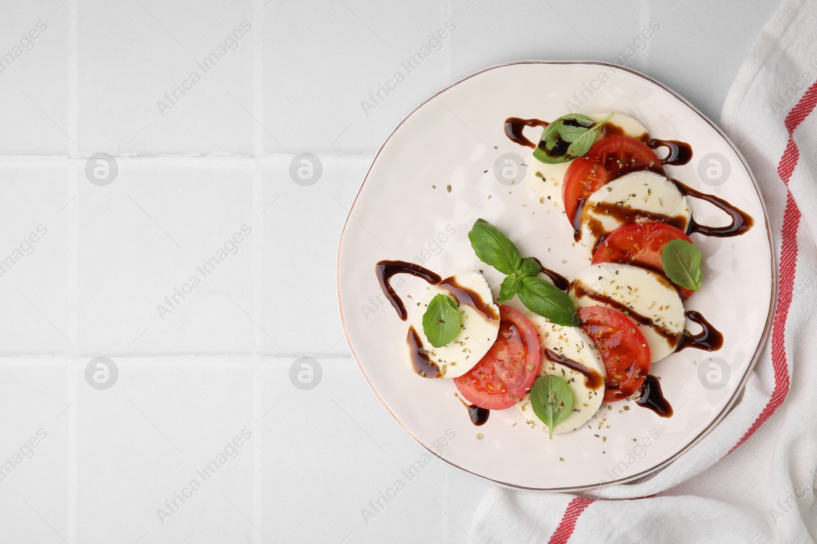 Photo of Delicious Caprese salad with balsamic vinegar on white tiled table, top view. Space for text