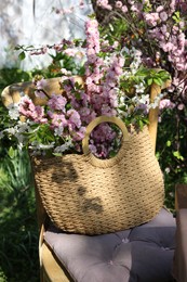 Photo of Wicker basket with beautiful spring flowers on chair in garden