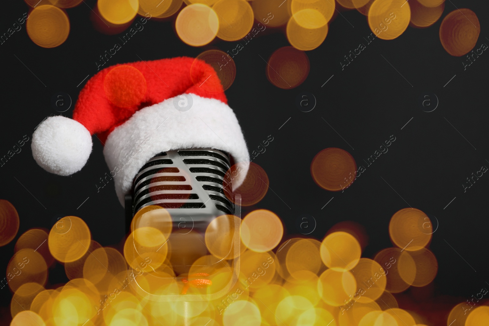 Image of Christmas music. Microphone with Santa hat on black background, bokeh effect