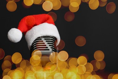 Christmas music. Microphone with Santa hat on black background, bokeh effect