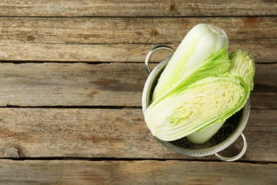 Whole and cut fresh Chinese cabbages in colander on wooden table, top view. Space for text