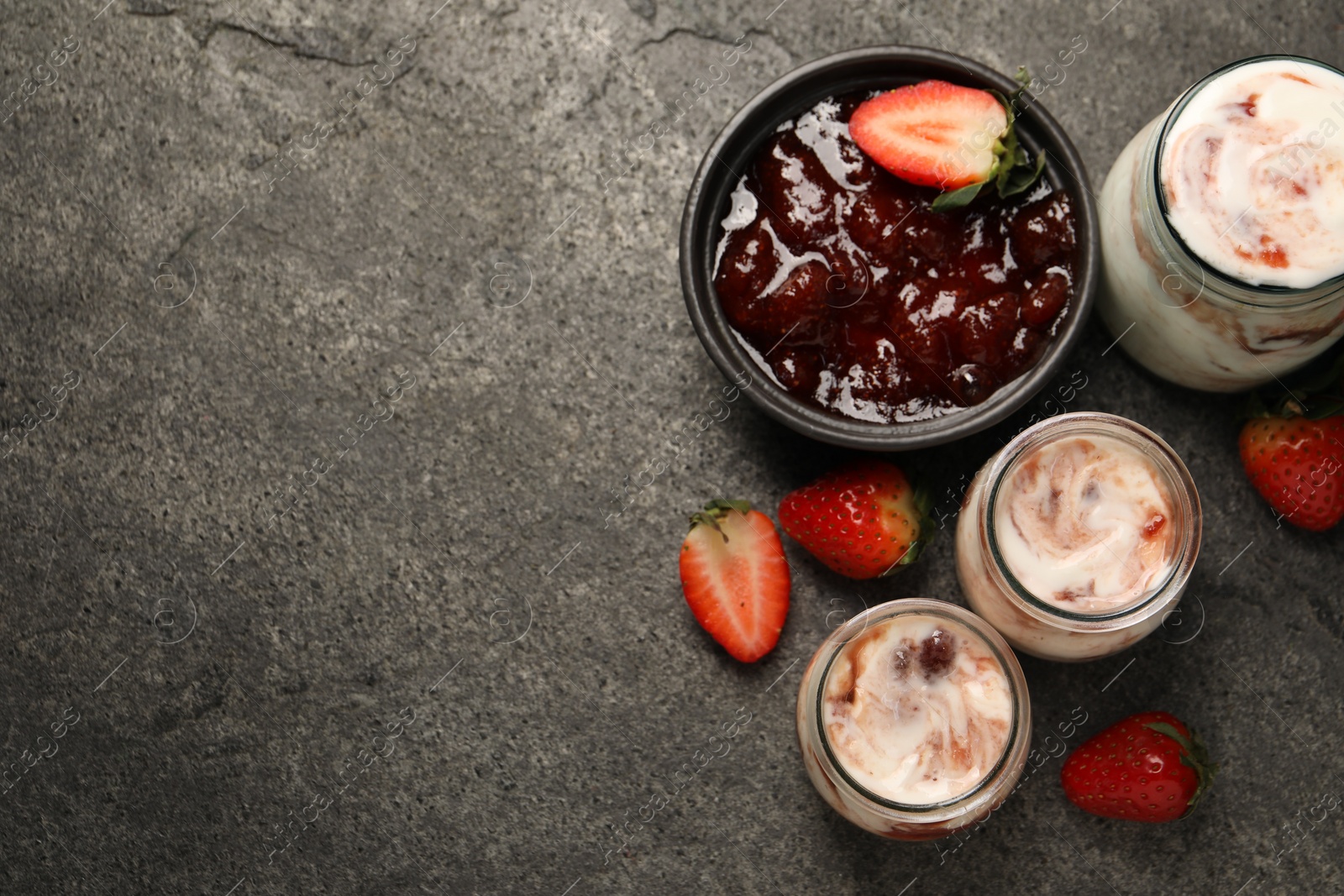 Photo of Tasty yoghurt with jam and strawberries on grey textured table, top view. Space for text