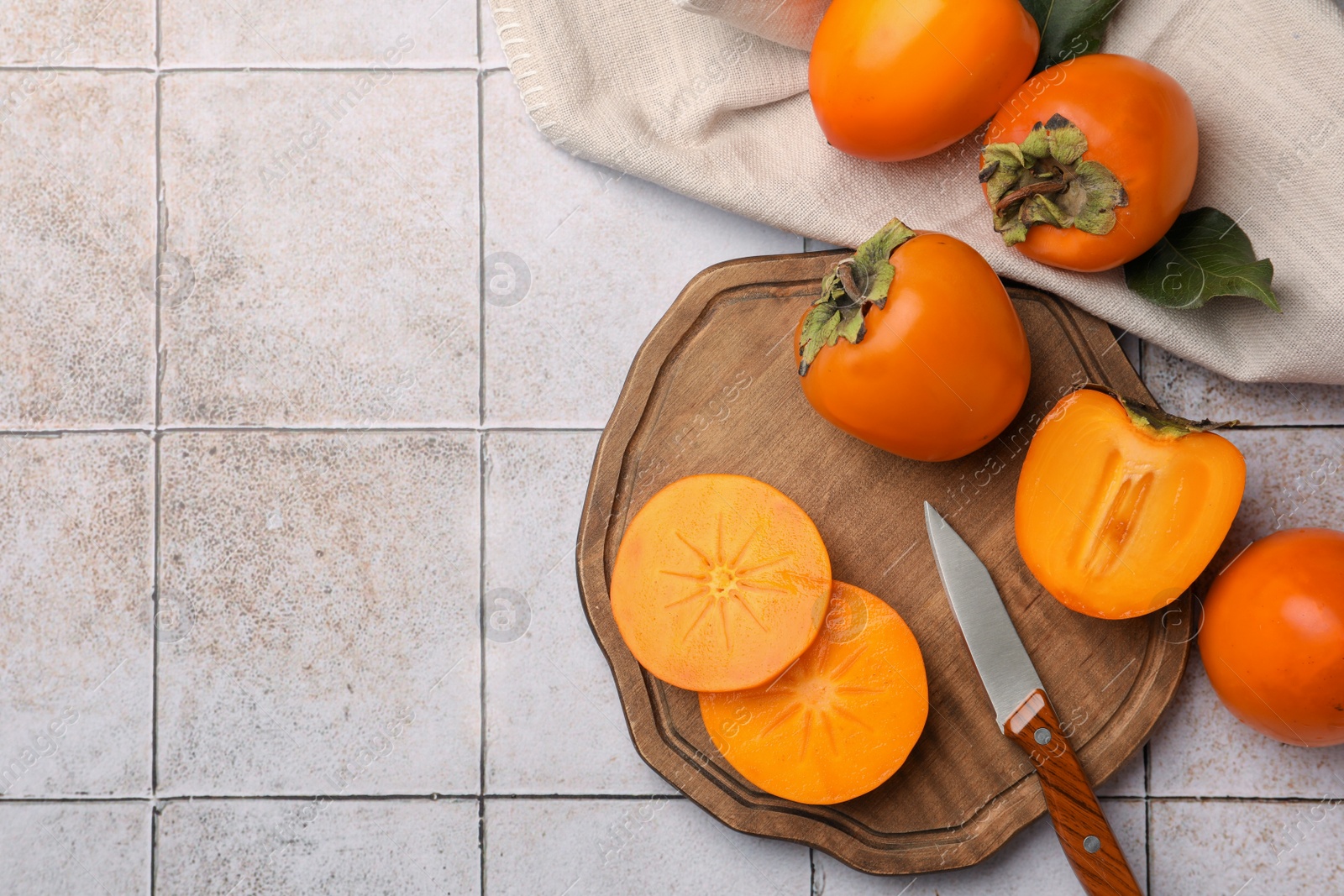 Photo of Delicious ripe juicy persimmons and knife on tiled surface, flat lay. Space for text