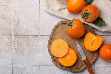 Delicious ripe juicy persimmons and knife on tiled surface, flat lay. Space for text