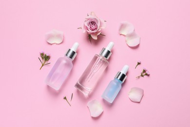 Bottles of cosmetic serums, flowers and petals on pink background, flat lay