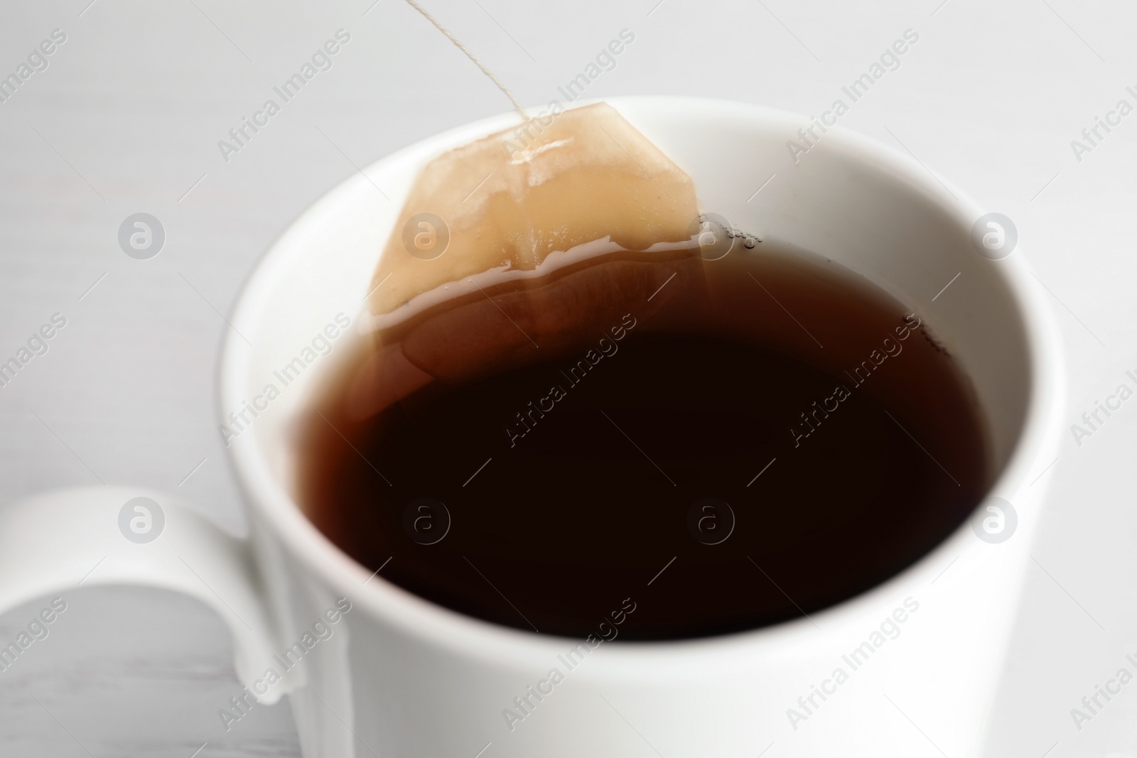 Photo of Teabag in cup with hot fresh drink, closeup