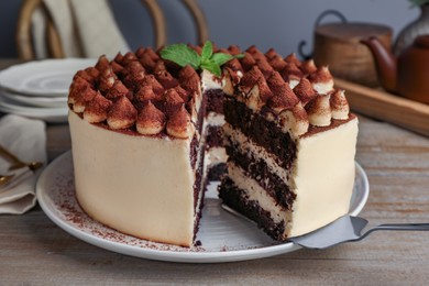 Photo of Delicious tiramisu cake with mint leaves and server on wooden table, closeup