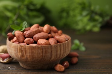 Photo of Fresh unpeeled peanuts in bowl on wooden table against blurred green background, closeup. Space for text