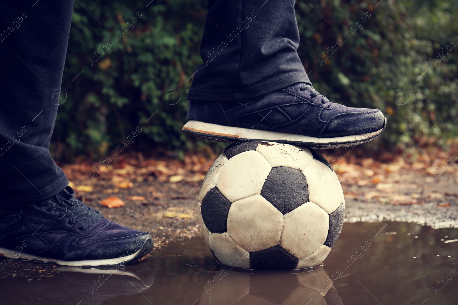 Photo of Man with soccer ball in muddy puddle outdoors, closeup