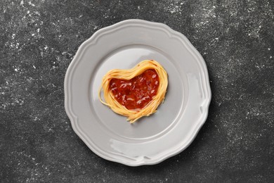 Photo of Heart made with spaghetti and sauce on black table, top view