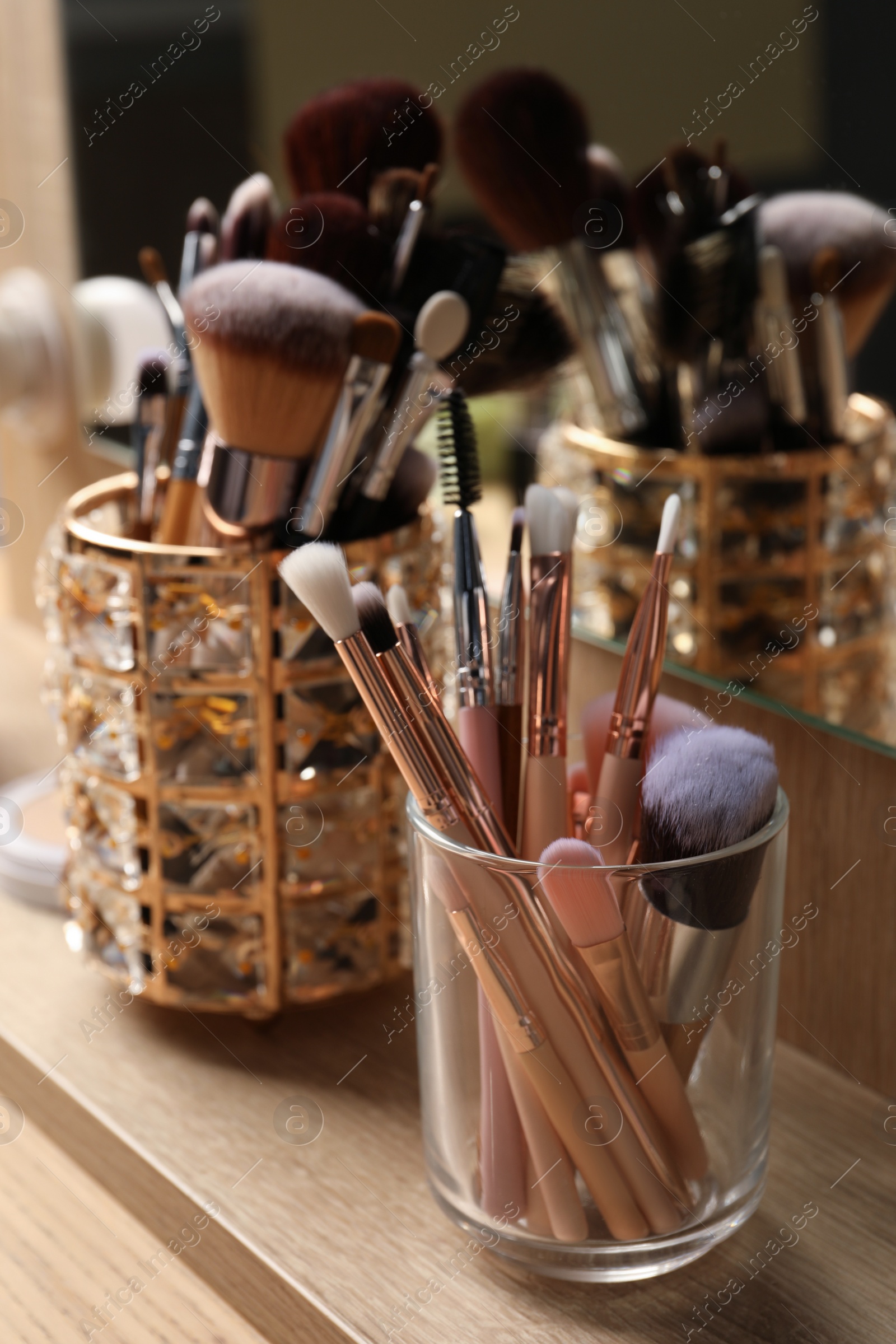 Photo of Set of professional makeup brushes near mirror on wooden table, closeup