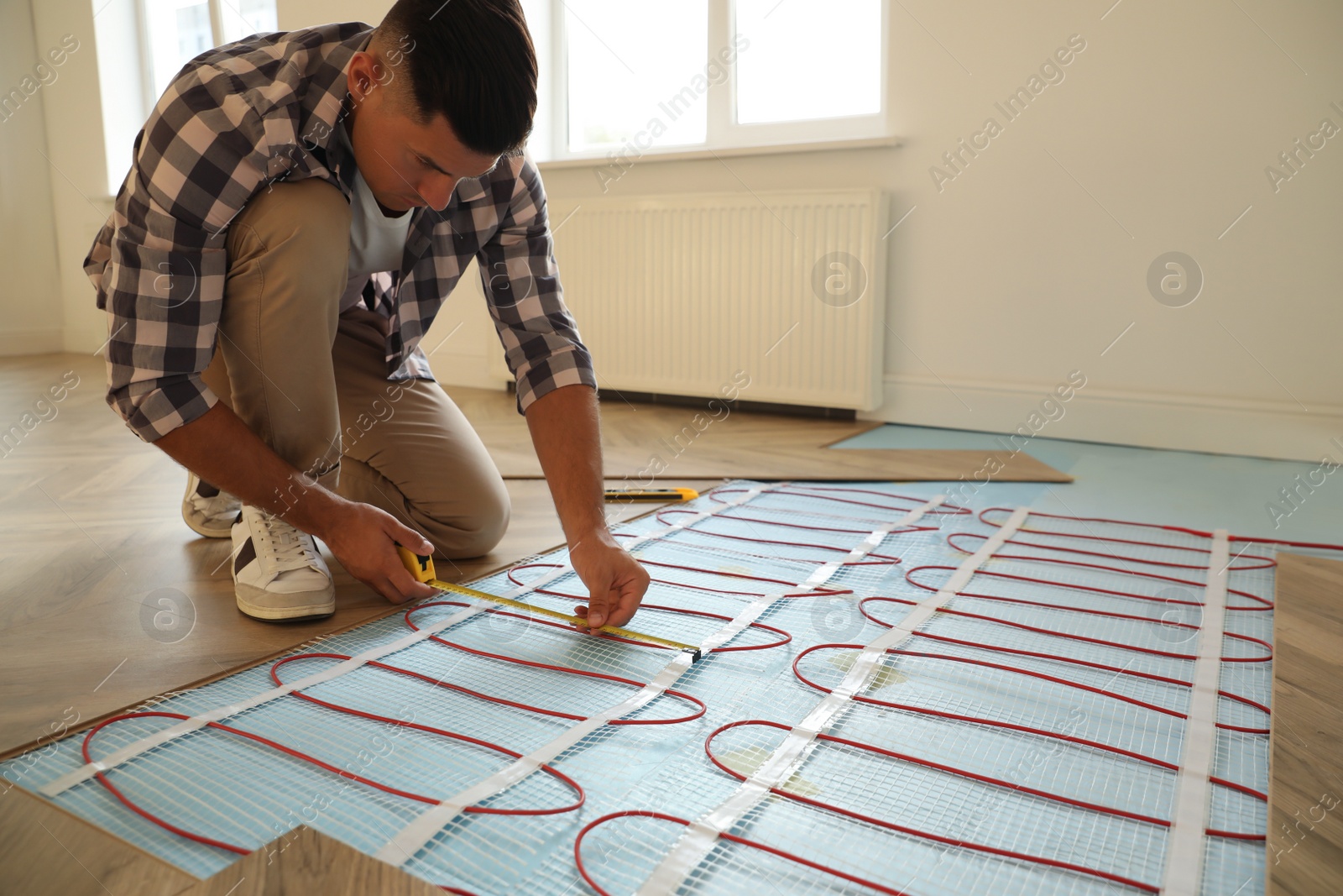 Photo of Professional worker installing electric underfloor heating system indoors