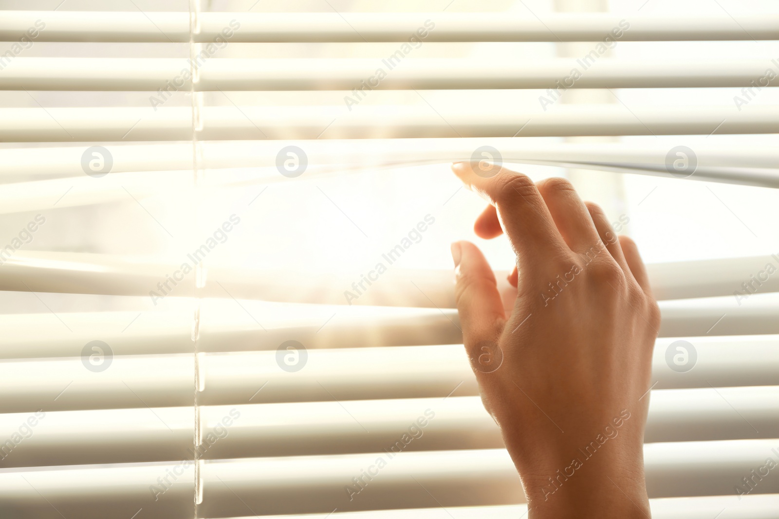 Image of Woman opening window blinds on sunny morning, closeup