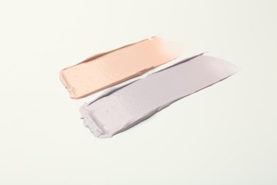Photo of Strokes of pink and purple color correcting concealers on white background