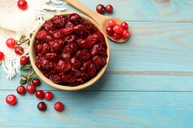 Photo of Tasty dried cranberries in bowl and fresh ones on light blue wooden table, top view. Space for text