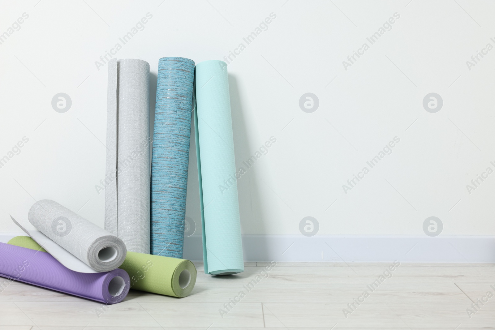 Photo of Different wallpaper rolls near white wall indoors, space for text