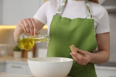 Photo of Making bread. Woman pouring oil into bowl at table in kitchen, closeup