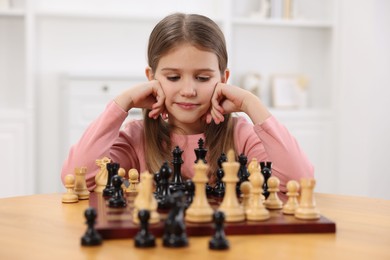 Cute girl playing chess at table in room