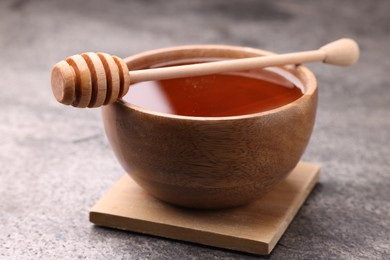 Photo of Delicious honey in bowl and dipper on grey textured table, closeup