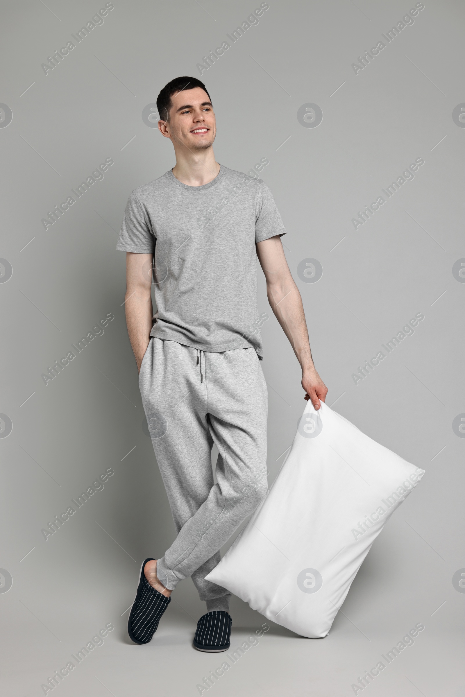 Photo of Happy man in pyjama holding pillow on grey background