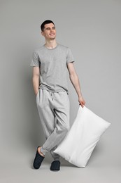 Happy man in pyjama holding pillow on grey background