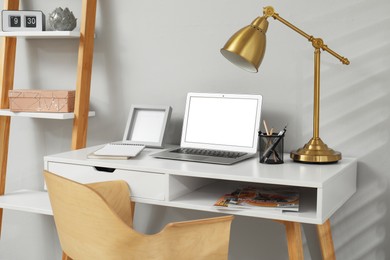 Comfortable workplace with modern laptop near light grey wall indoors