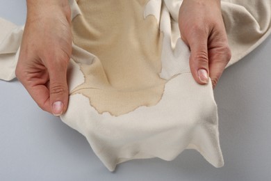 Photo of Woman holding beige sweater with stain on light grey background, top view