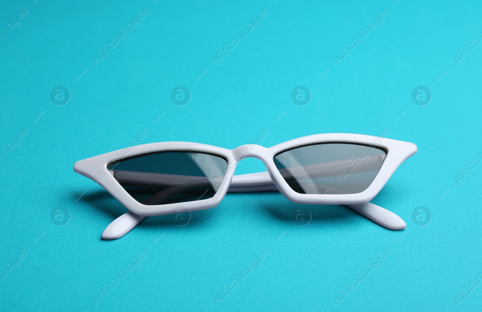 Photo of Stylish sunglasses on blue background. Fashionable accessory