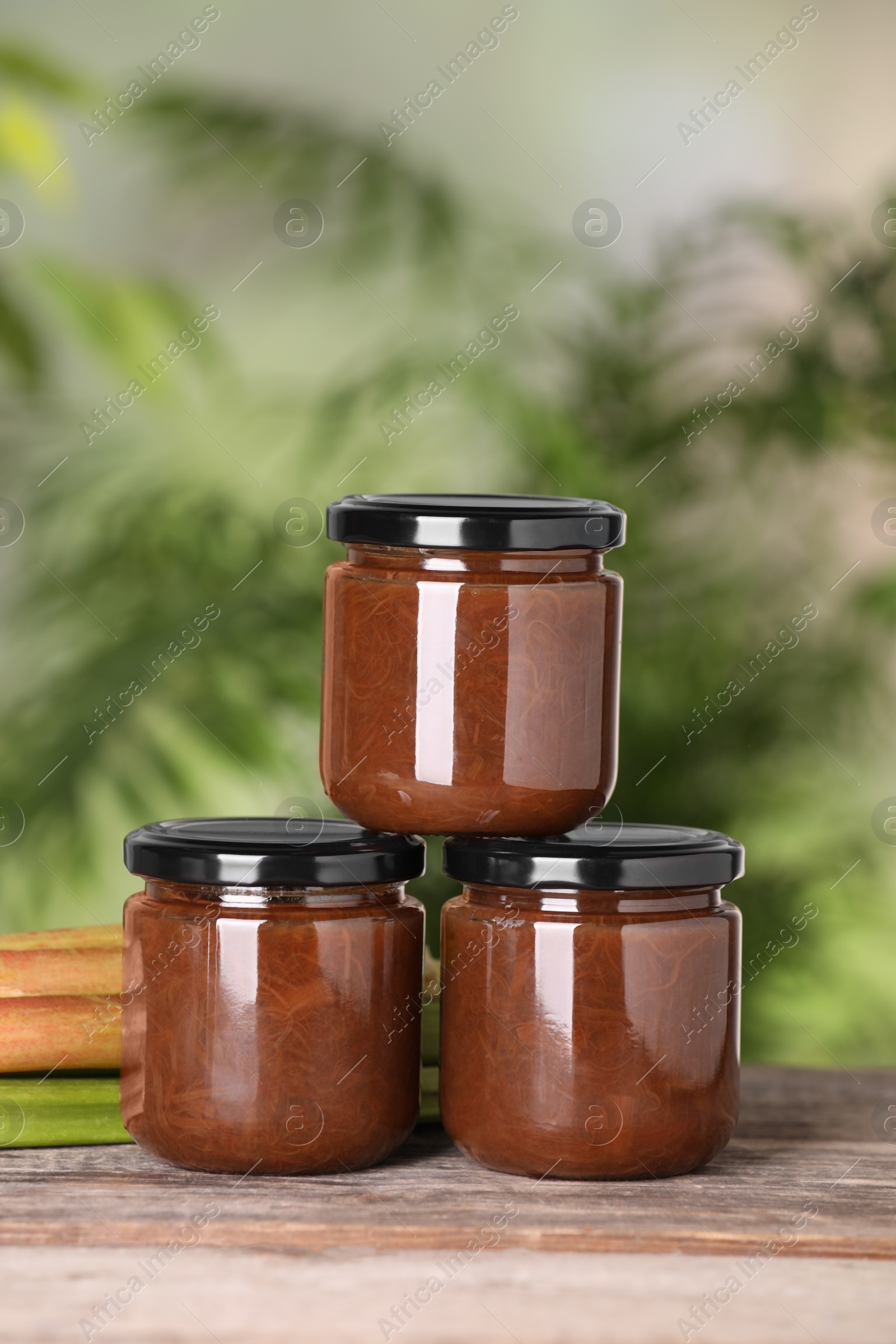 Photo of Jars of tasty rhubarb jam on wooden table, closeup