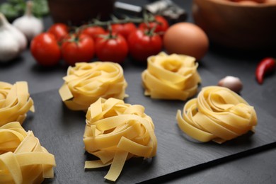 Uncooked tagliatelle and fresh ingredients on black table, closeup