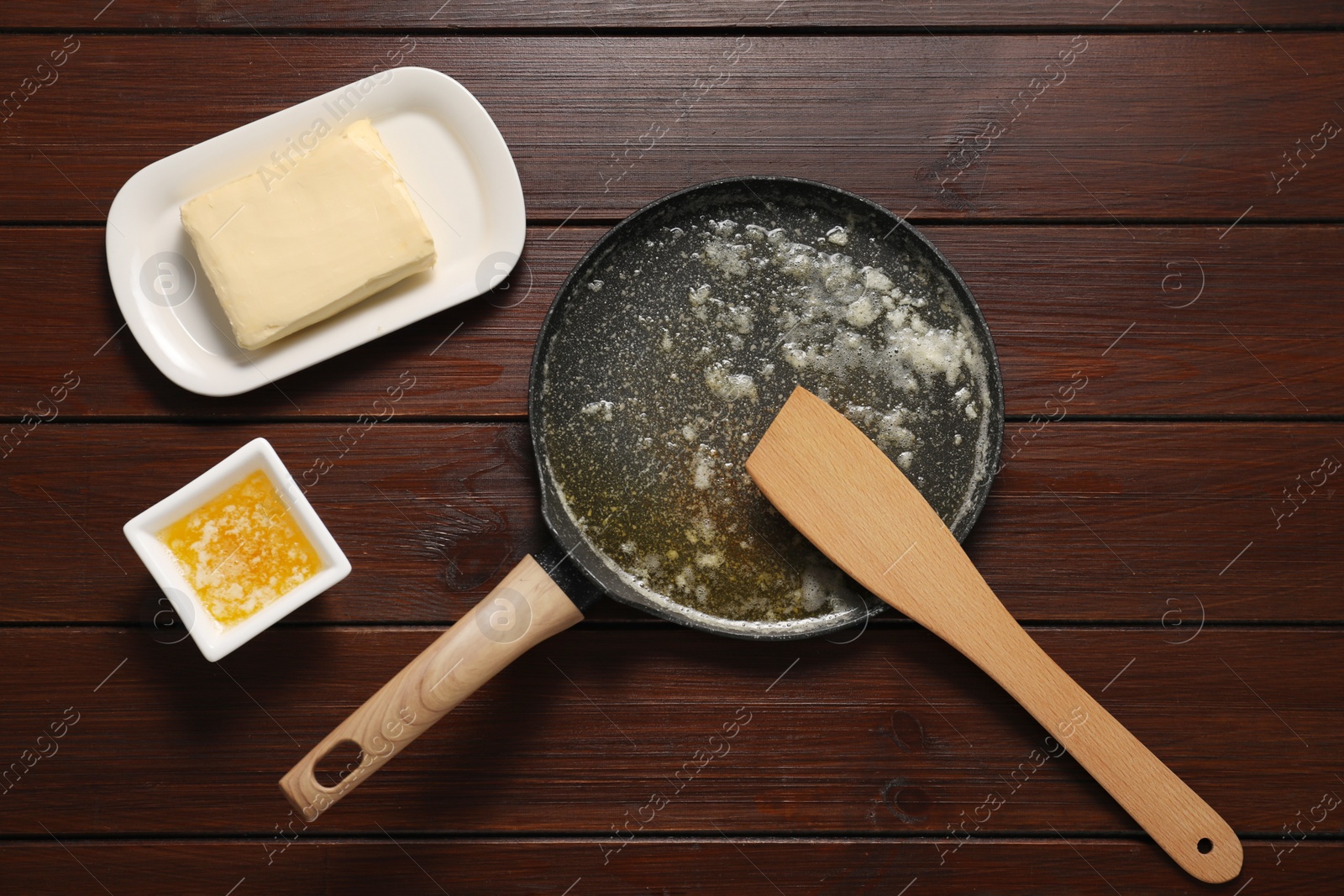 Photo of Melted butter in frying pan and spatula on wooden table, flat lay