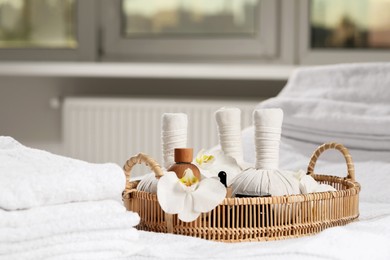 Photo of Wicker tray with herbal bags and other spa products on white bath towel. Space for text