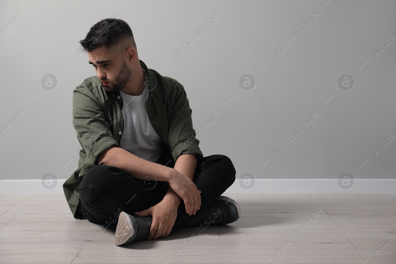 Photo of Sad man sitting on floor near light grey wall. Space for text