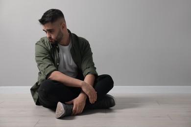 Sad man sitting on floor near light grey wall. Space for text