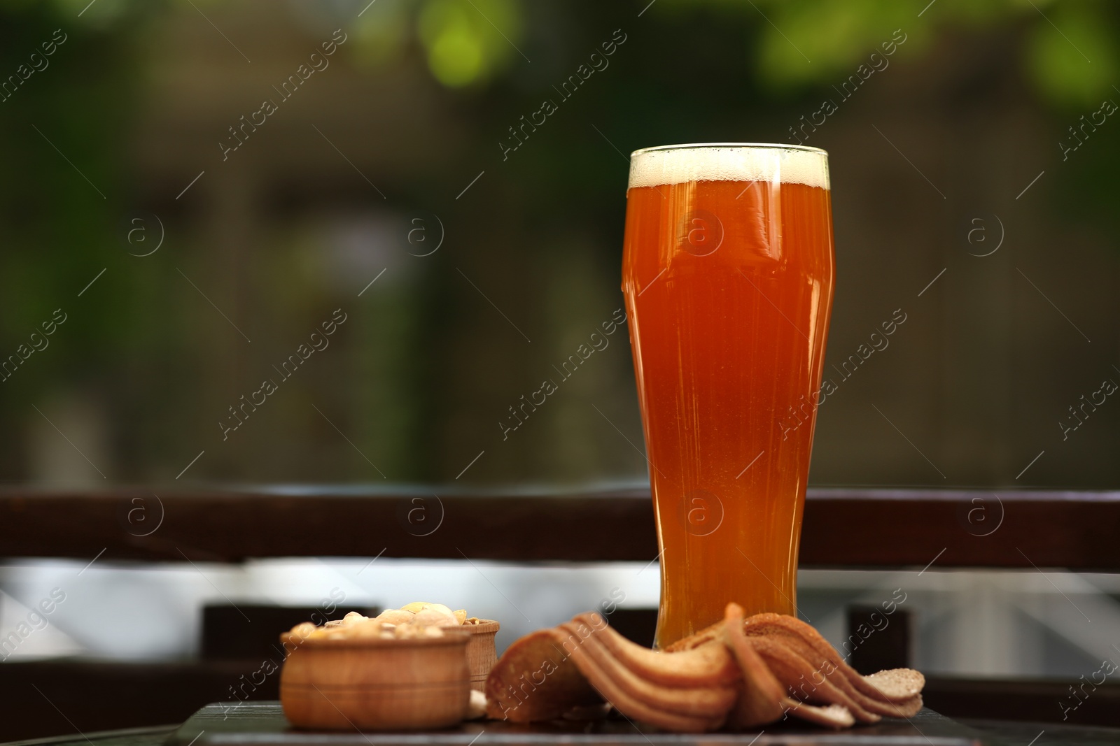 Photo of Glass of tasty beer served with snacks on table outdoors, space for text