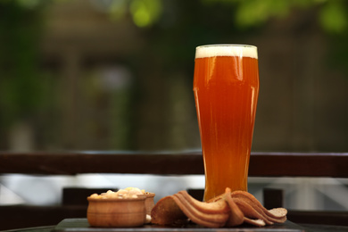 Glass of tasty beer served with snacks on table outdoors, space for text