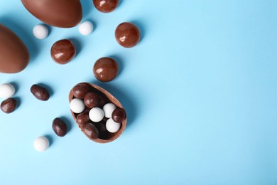 Photo of Tasty chocolate eggs and different sweets on light blue background, flat lay with space for text