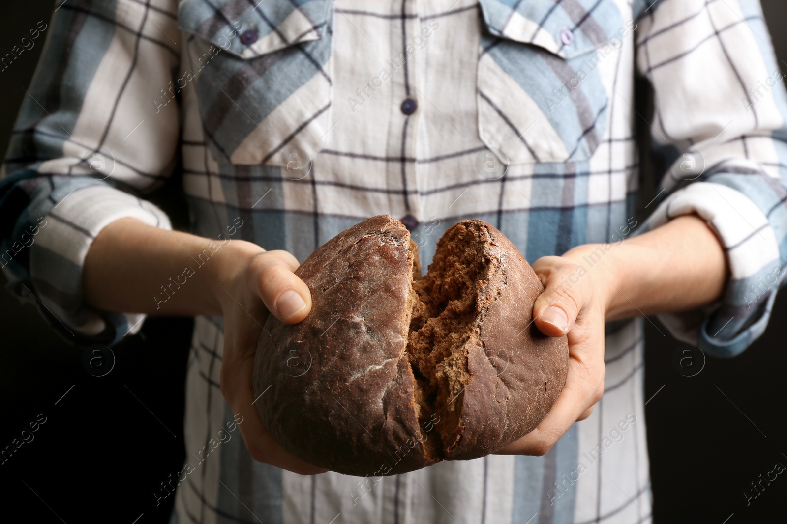 Photo of Woman breaking freshly baked bread on black background, closeup