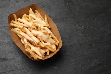 Photo of Tasty potato fries and cheese sauce in paper container on black table, top view. Space for text